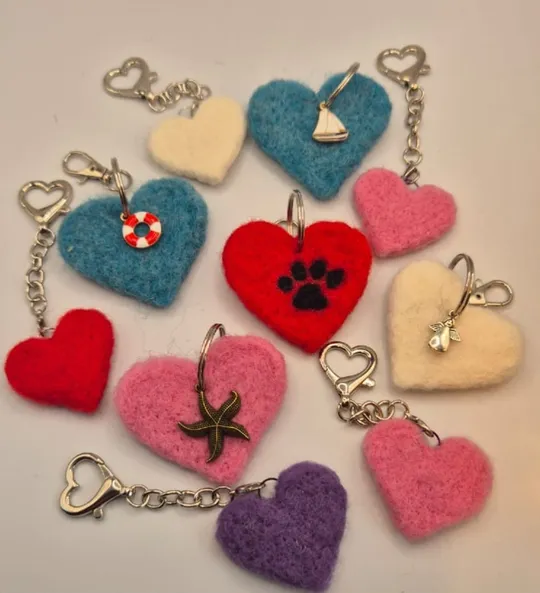 Ein Dutzend gefilzte Schlüsselanhänger in Herzform in Rot, Rosa, Blau, Weiß und Lila, teils mit Anhängern wie Hundepfote, Seestern und Segelboot.